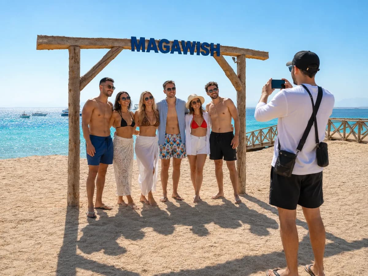 Friends taking a selfie under the MAGAWISH island sign with the golden heart photo frame and turquoise Red Sea behind, on a Magawish and Orange Bay day trip from Hurghada